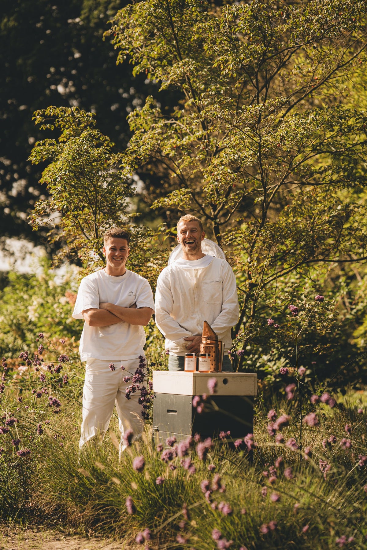 Twee imkers naast een bijenkast in een bloeiende tuin